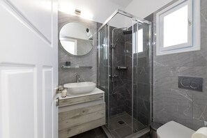 A modern bathroom with a glass-enclosed shower, a white sink, and a marble-tiled wall. - Eutuxia Rooms & Studios (Sifnos)