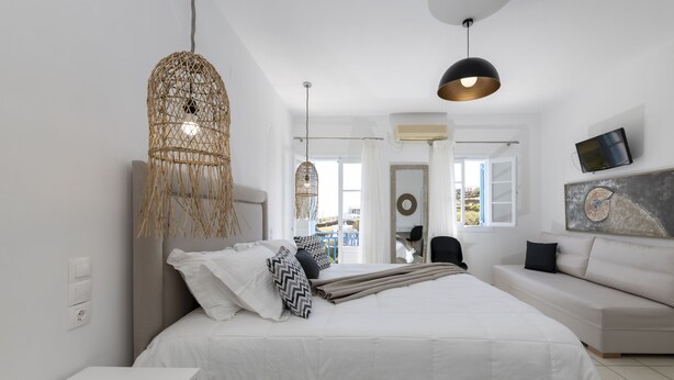 Un dormitorio moderno con una cama grande, un sofá, un televisor y una lámpara colgante.