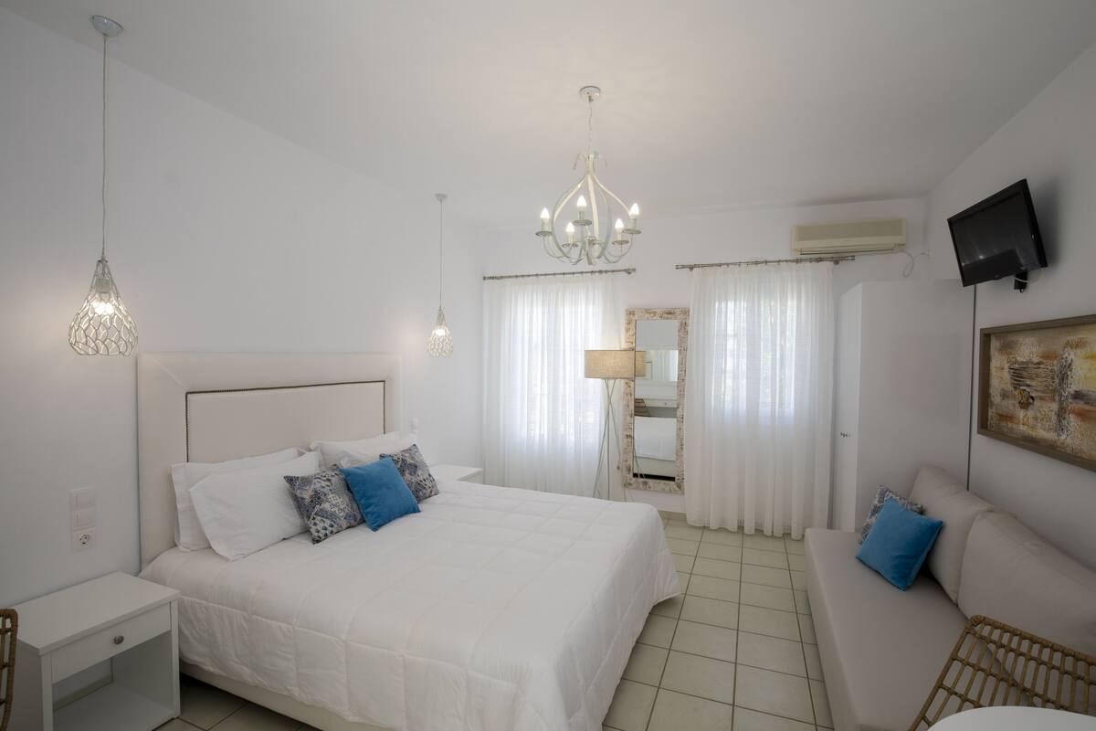 A bedroom with a bed, a nightstand, a bedside table, a sofa, a television, and a chandelier.