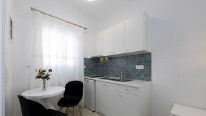 Una cocina compacta con armarios blancos, encimera negra y un pequeño comedor con dos sillas y una mesa.