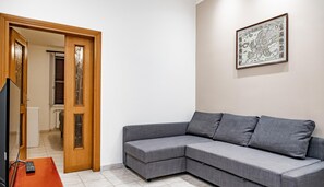 A modern living room with a grey sectional sofa, a wooden door with glass panels, and a framed map on the wall. - Mecenate Apartment Cavour (Rome)