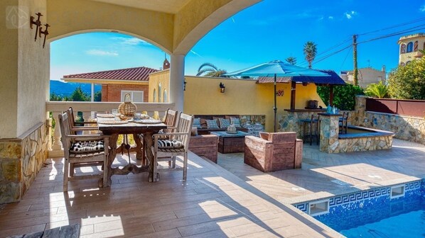 An outdoor patio with a pool, stone seating, and a table set for dining.