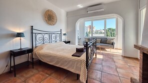 Une chambre à coucher comprenant un lit, des tables de chevet, une lampe, un élément décoratif mural et une vue sur l’extérieur par une fenêtre.