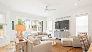 A spacious living room with a large flat-screen TV, a ceiling fan, and a view of the outside. - Steps to Beach w/ Kayak, Pool and LSV (Santa Rosa Beach)