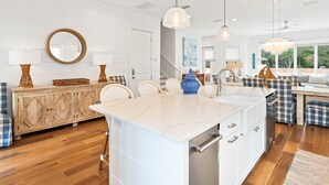 A modern kitchen with a central island, white cabinetry, and a dining area with a checkered bench. - Steps to Beach w/ Kayak, Pool and LSV (Santa Rosa Beach)