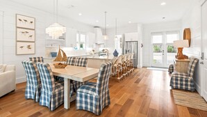 A modern kitchen with white cabinetry, a central island, and a dining area with checkered chairs. - Steps to Beach w/ Kayak, Pool and LSV (Santa Rosa Beach)