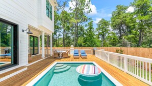 A swimming pool with lounge chairs and a wooden deck, surrounded by a wooden fence and trees. - Steps to Beach w/ Kayak, Pool and LSV (Santa Rosa Beach)