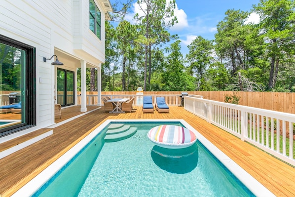 A swimming pool with lounge chairs and a wooden deck, surrounded by a wooden fence and trees.
