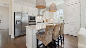A modern kitchen with white cabinetry, stainless steel appliances, a central island with bar stools, and pendant lighting. - GORGEOUS Highland Parks w LSV & Bikes! Loaded 30A Home! (Santa Rosa Beach)