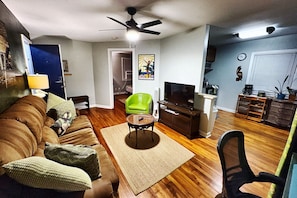 A living room with a brown sofa, a green chair, a TV, and a ceiling fan.