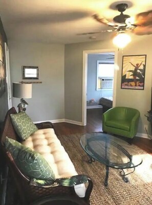 Een woonkamer met een bank, een glazen salontafel en een groene fauteuil.