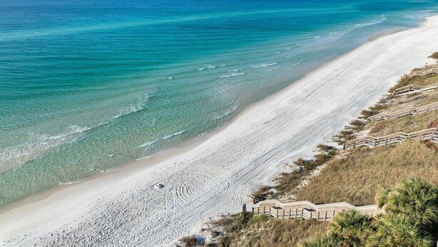 Een strand met helder turquoise water, een zandstrand en houten looppaden.
