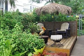 Una terraza de madera con dos sillas y una mesa, rodeada de abundante vegetación y una estructura de techo de paja.