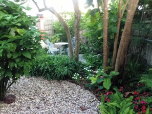 A garden with a gravel path, various plants, and a small table with chairs.
