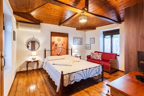 Ein Schlafzimmer mit Holzbalkendecke, einem Bett mit weißer Bettdecke, einem roten Sofa, einem Fernseher und einem Holzboden.