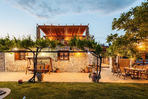 Ein Steingebäude mit einer Holzpergola, Außenplätzen und Topfpflanzen.