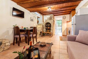 A cozy living area with a stone fireplace, wooden ceiling, and a dining table with chairs. - Petalidi Olive Garden Stone House near the beach (Petalidi)