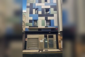 A modern building with a geometric facade, a ground-level entrance with a closed shutter, and a visible sign indicating a loft apartment. - LA CICER BEACH APARTMENT ll (Palmas De Gran Canaria, Las)