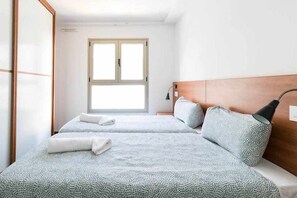 A hotel room with two beds, a window, a bedside lamp, and a wooden headboard. - LA CICER BEACH APARTMENT ll (Palmas De Gran Canaria, Las)