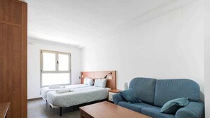 A hotel room with a bed, a sofa, a wooden table, and a window. - LA CICER BEACH APARTMENT ll (Palmas De Gran Canaria, Las)