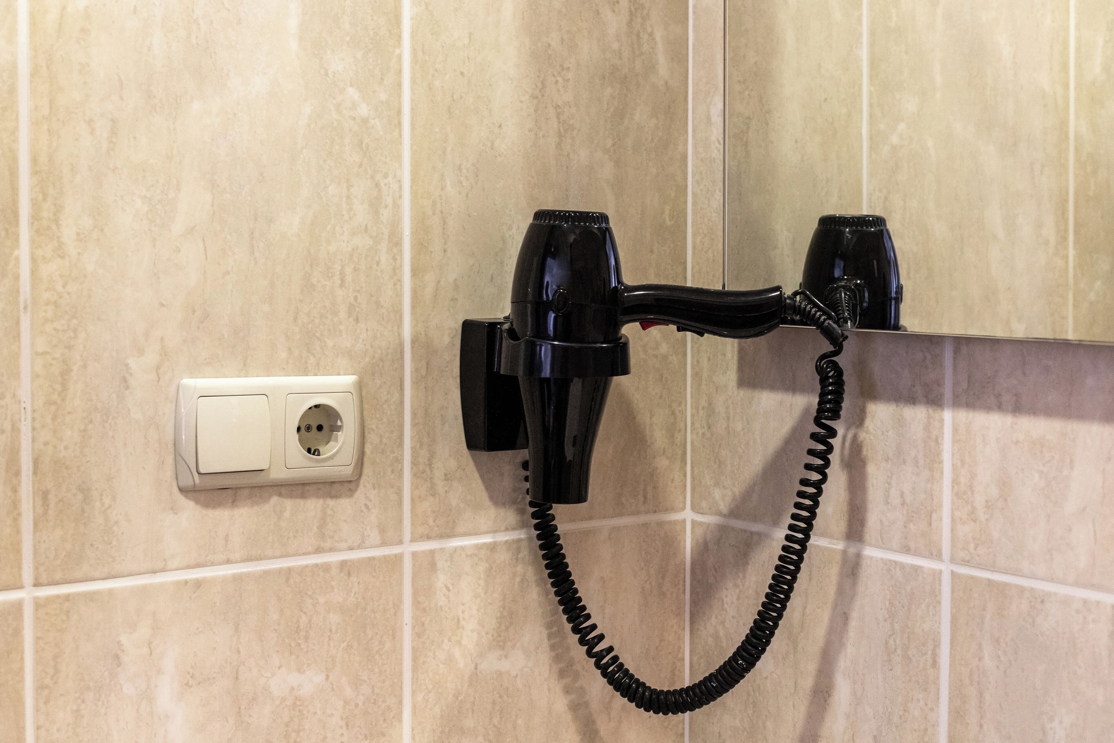 A hairdryer mounted on a tiled wall with a power outlet nearby.