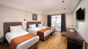 Habitación de hotel con dos camas, un escritorio, televisor y balcón con vistas.