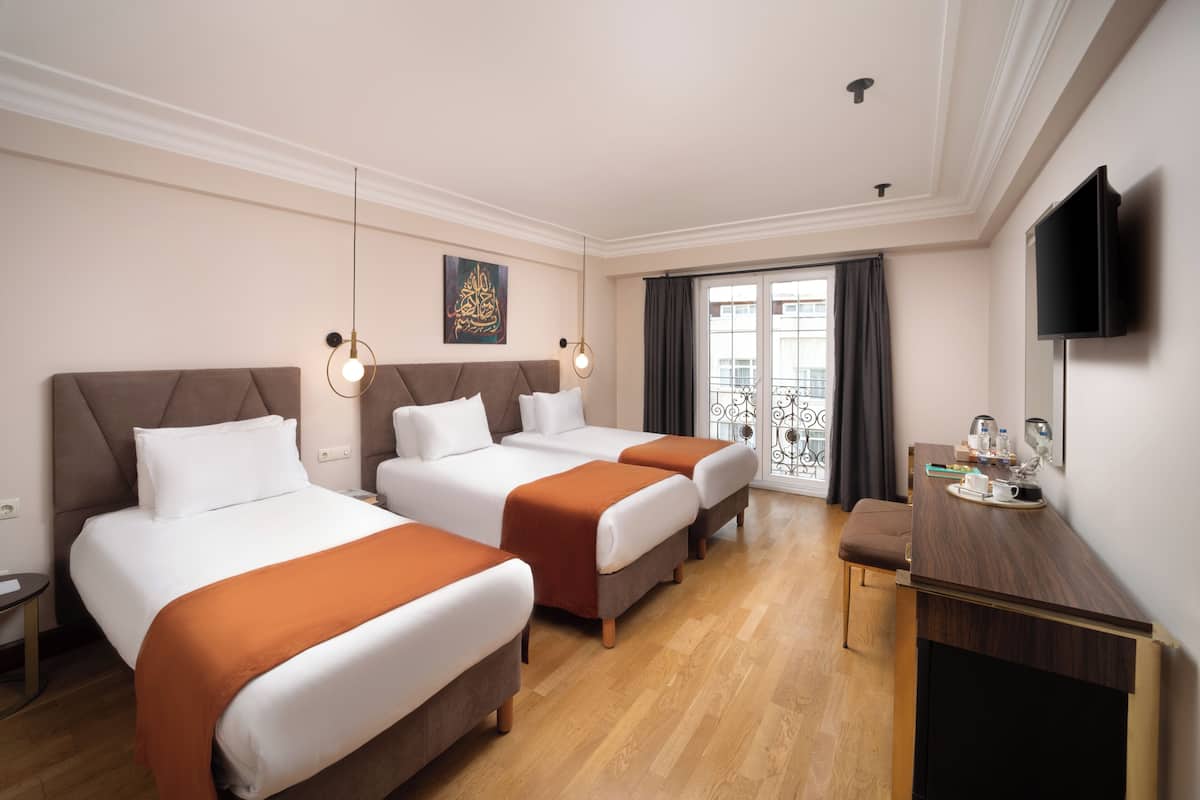 A hotel room with two beds, a desk, a TV, and a balcony with a view.