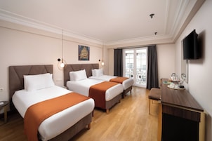 Habitación de hotel con dos camas, un escritorio, televisor y balcón con vistas.