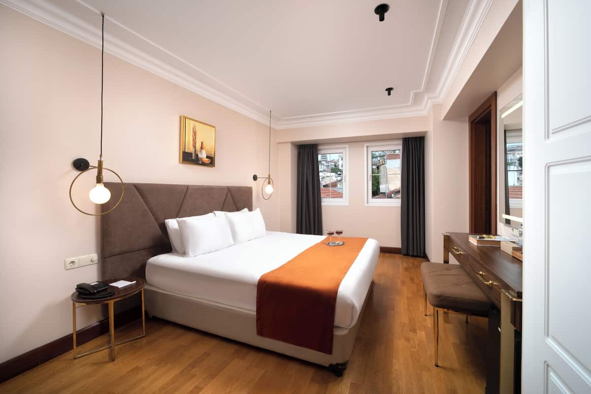 A neatly arranged hotel room with a large bed, bedside table, and a desk with a chair.