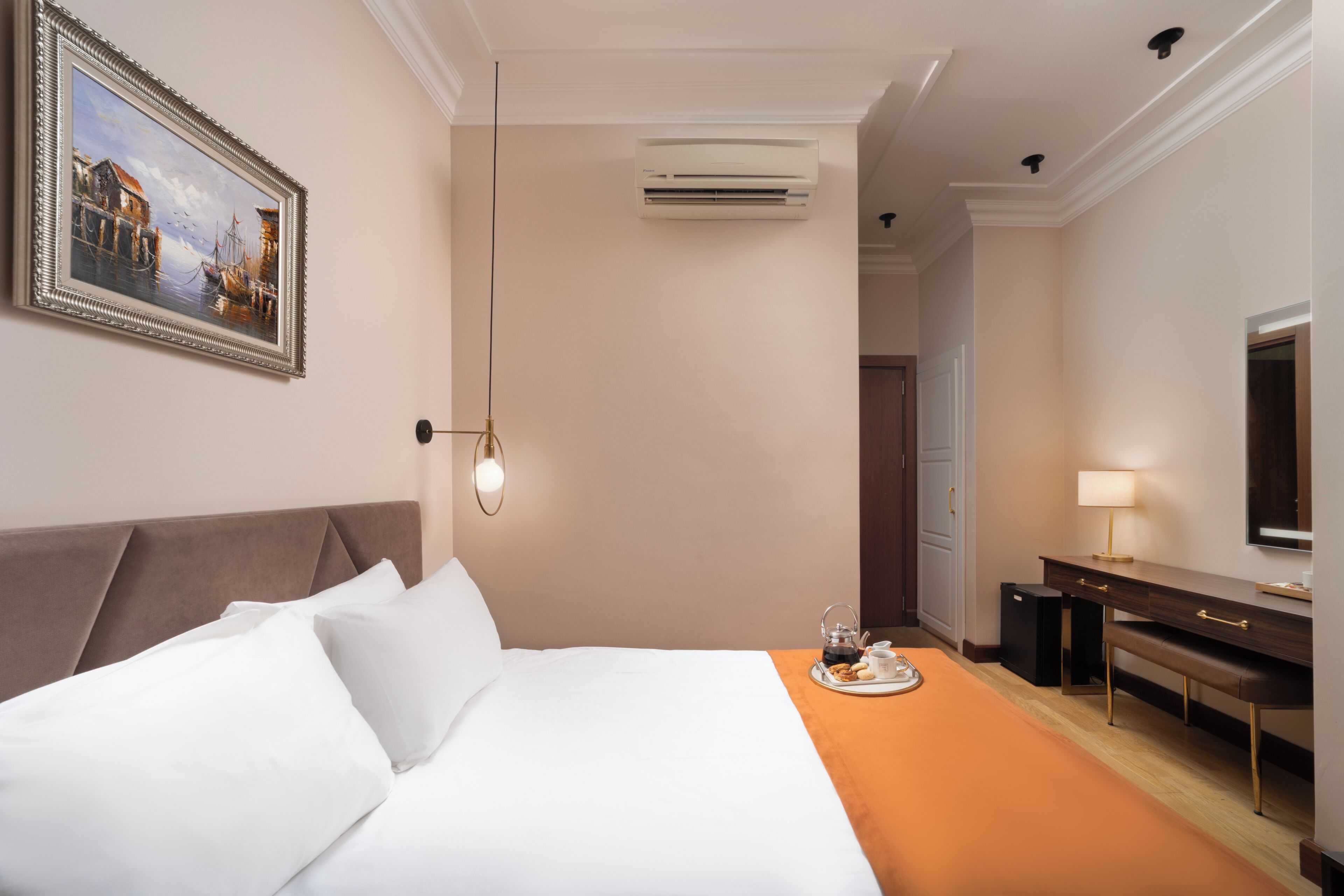 Une chambre d’hôtel comprenant un lit, un tableau, un appareil de climatisation, un bureau avec une lampe et un téléviseur.