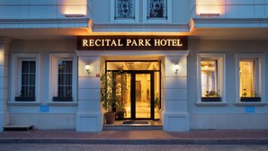 Exterior del Hotel Recital Park con una entrada destacada, plantas en macetas y una fachada bien iluminada.