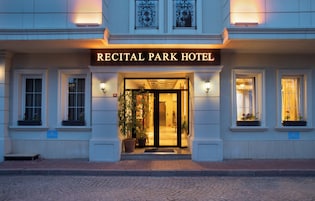 Exterior del Hotel Recital Park con una entrada destacada, plantas en macetas y una fachada bien iluminada.