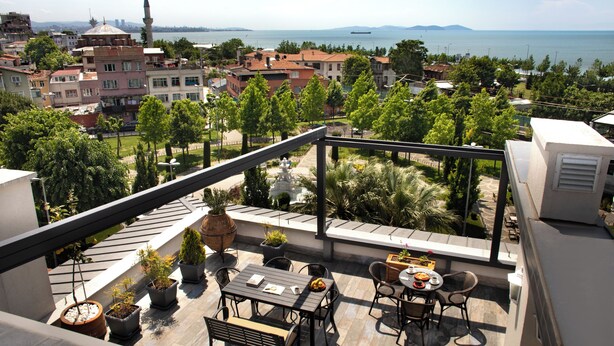 Una terraza en la azotea con zona de comedor, plantas en macetas y vistas a la ciudad y al mar.