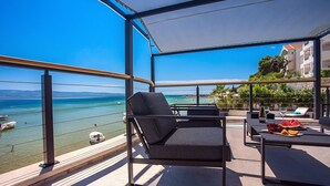 A balcony with a view of the sea, a chair, a table with a bottle and glasses, and a plate of fruit. - Beachfront Villa Draga with 32sqm private, heated pool, 4 bedrooms, sea view (Omis)
