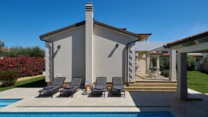 Et moderne hus med swimmingpool, liggestole og en overdækket terrasse.