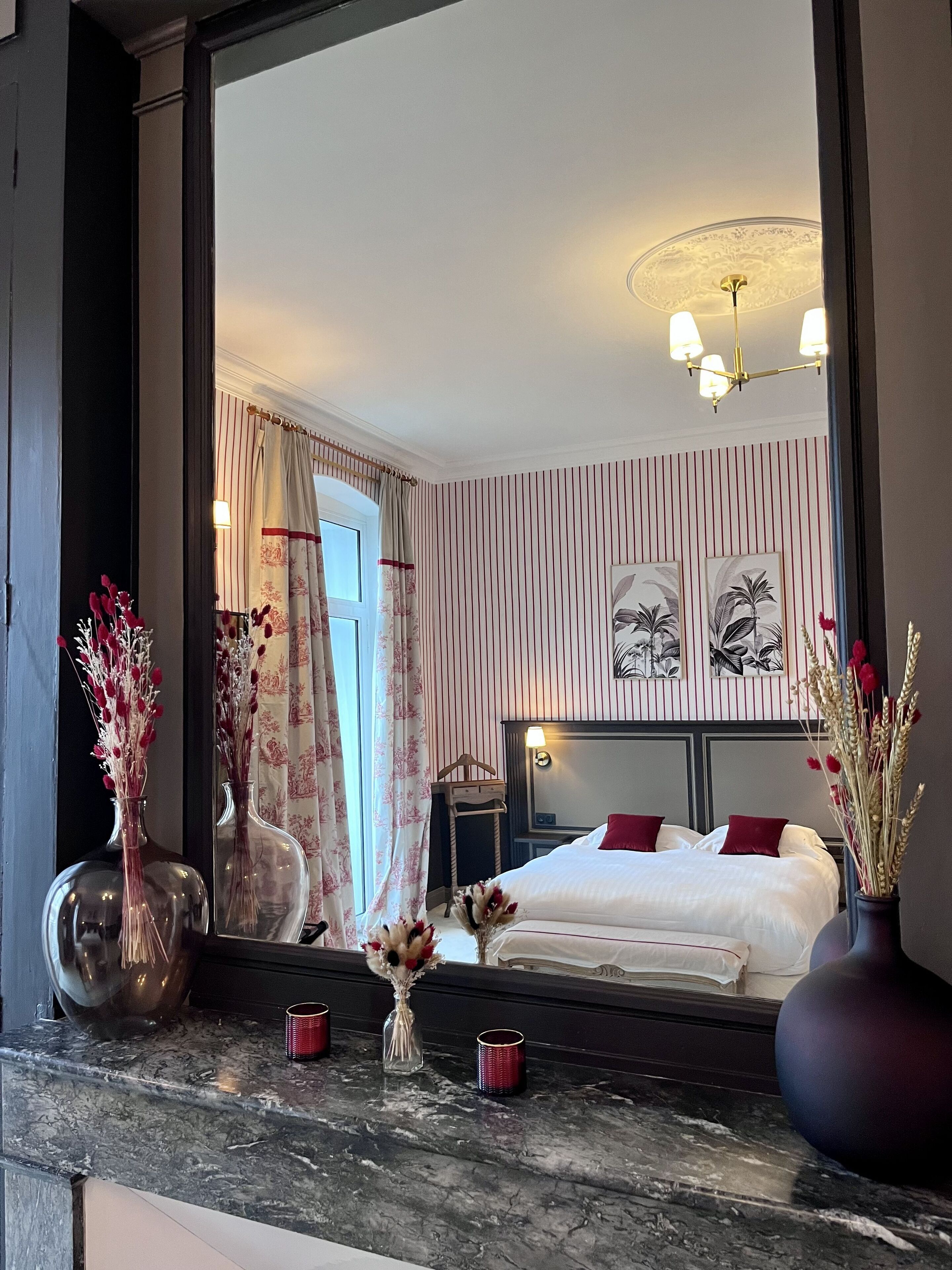 A hotel room with a large bed, a nightstand, a mirror, and a marble countertop with decorative items.