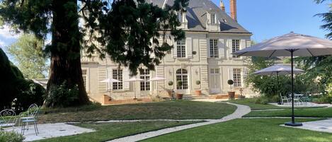 Una casa grande e histórica con un césped cuidado, mobiliario exterior y un camino de grava que lleva a la entrada.