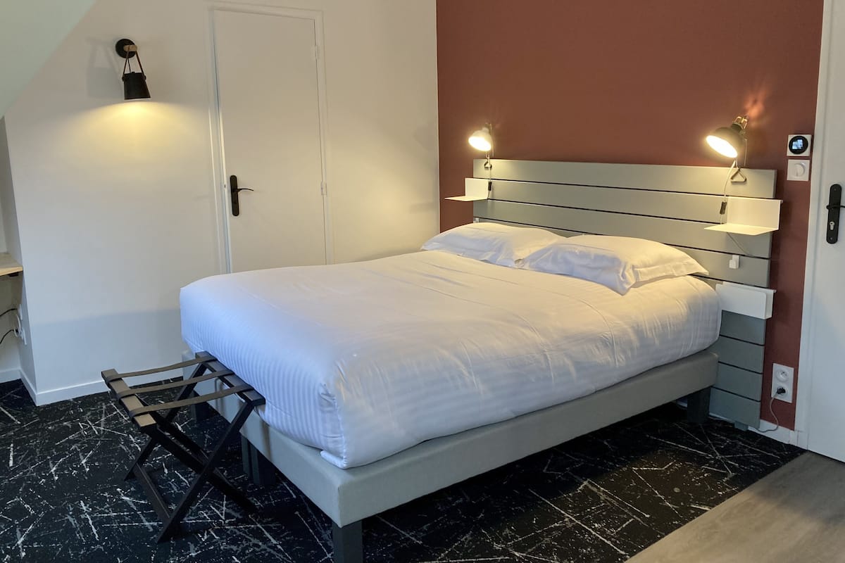 A neatly made bed with white linens, a headboard with integrated lighting, a small bedside table, and a wall-mounted nightstand.