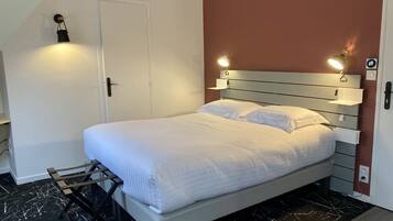 Een netjes opgemaakt bed met witte lakens, een hoofdbord met ingebouwde verlichting, een klein nachtkastje en een wandlamp.
