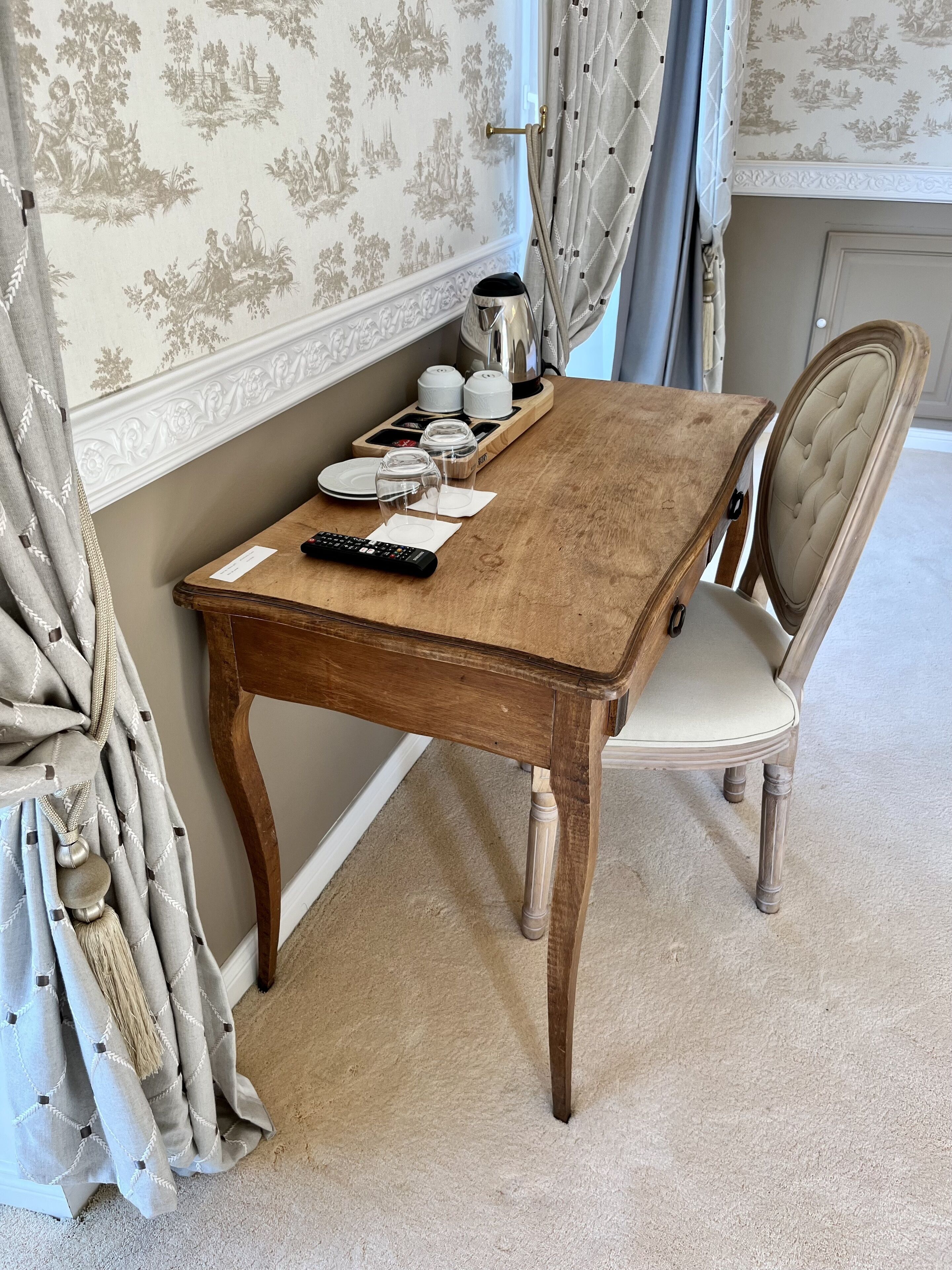 A wooden dining table with a remote control, a kettle, and glass jars on a tray.