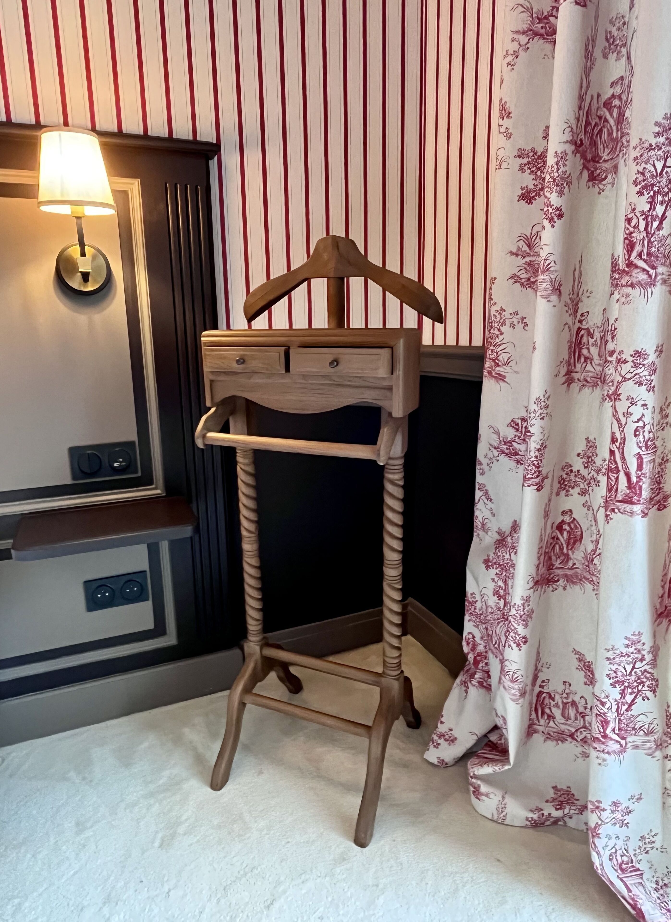 Une petite table d’appoint en bois, dotée d’une étagère suspendue, d’une lampe et d’un rideau orné d’un motif floral.