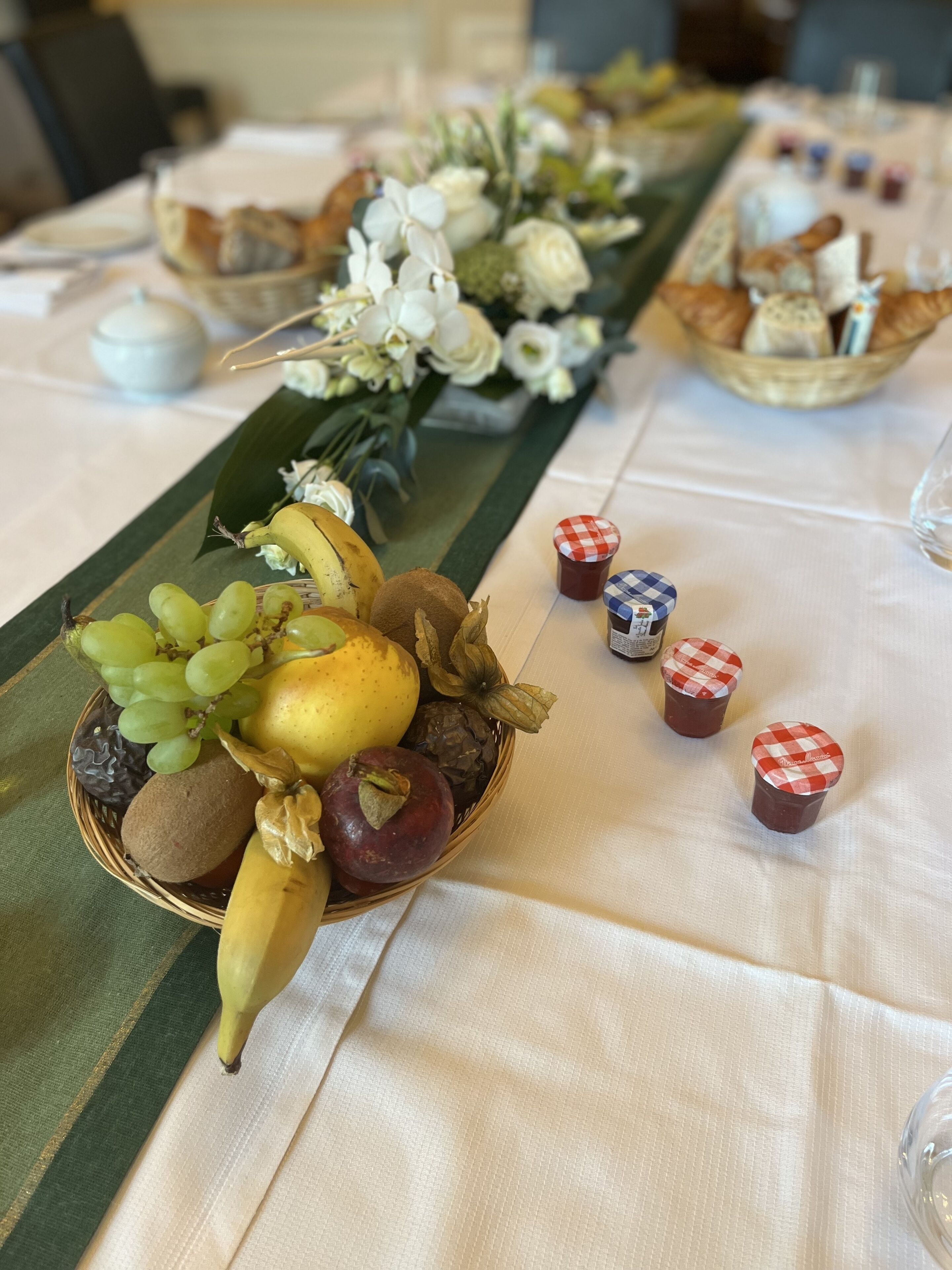 Une table avec un panier de fruits, une composition florale et de petits récipients dotés de couvercles à carreaux.