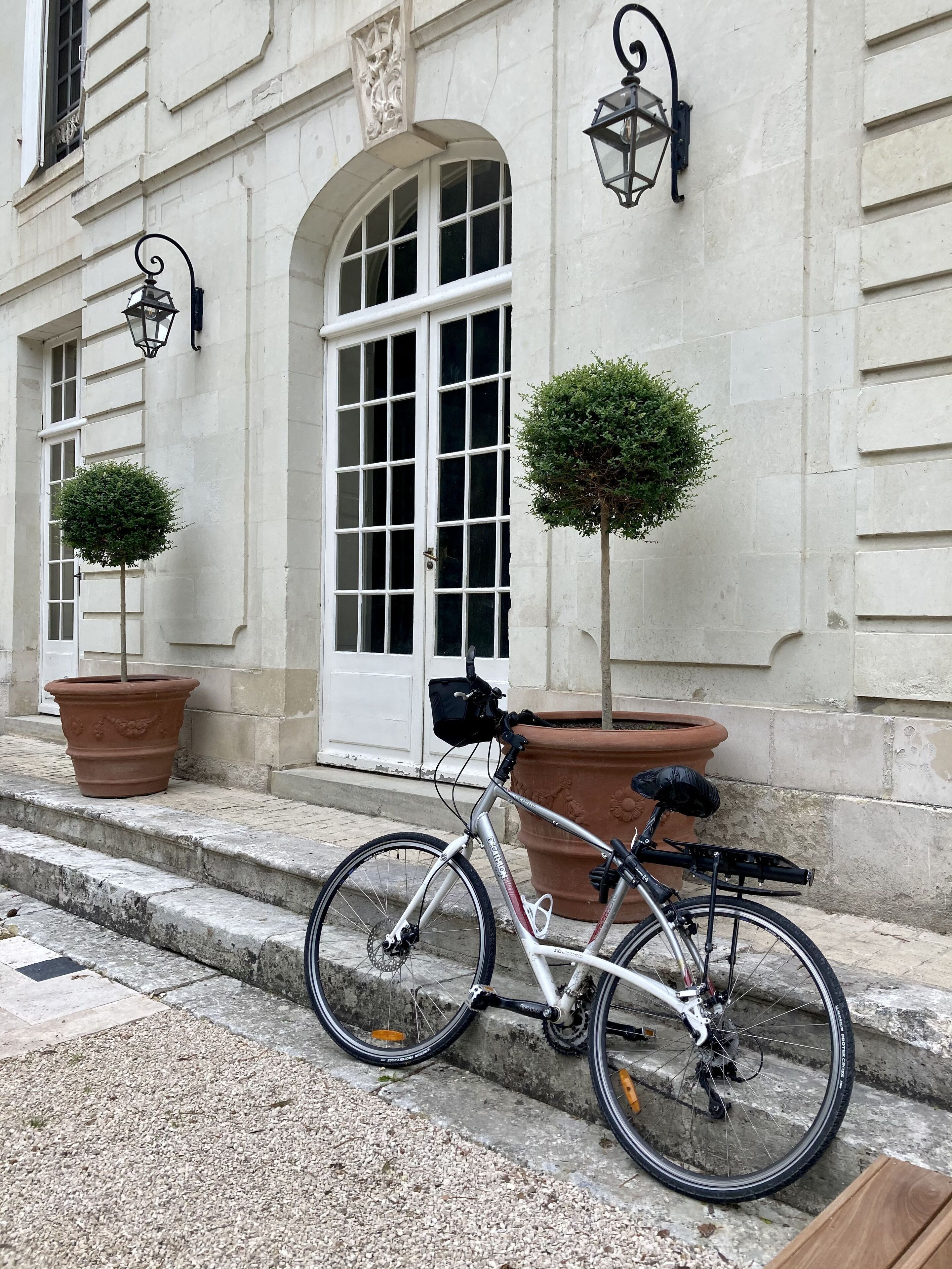Ein Fahrrad steht auf einer Steinstufenanlage neben einem Gebäude mit einer weißen Tür und zwei Blumentöpfen.