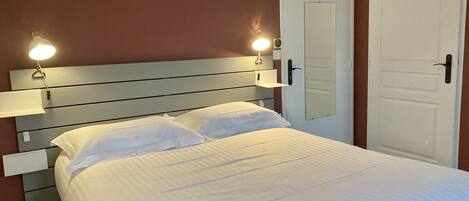 A neatly made bed with white linens in a room with a wooden headboard and two bedside lamps.