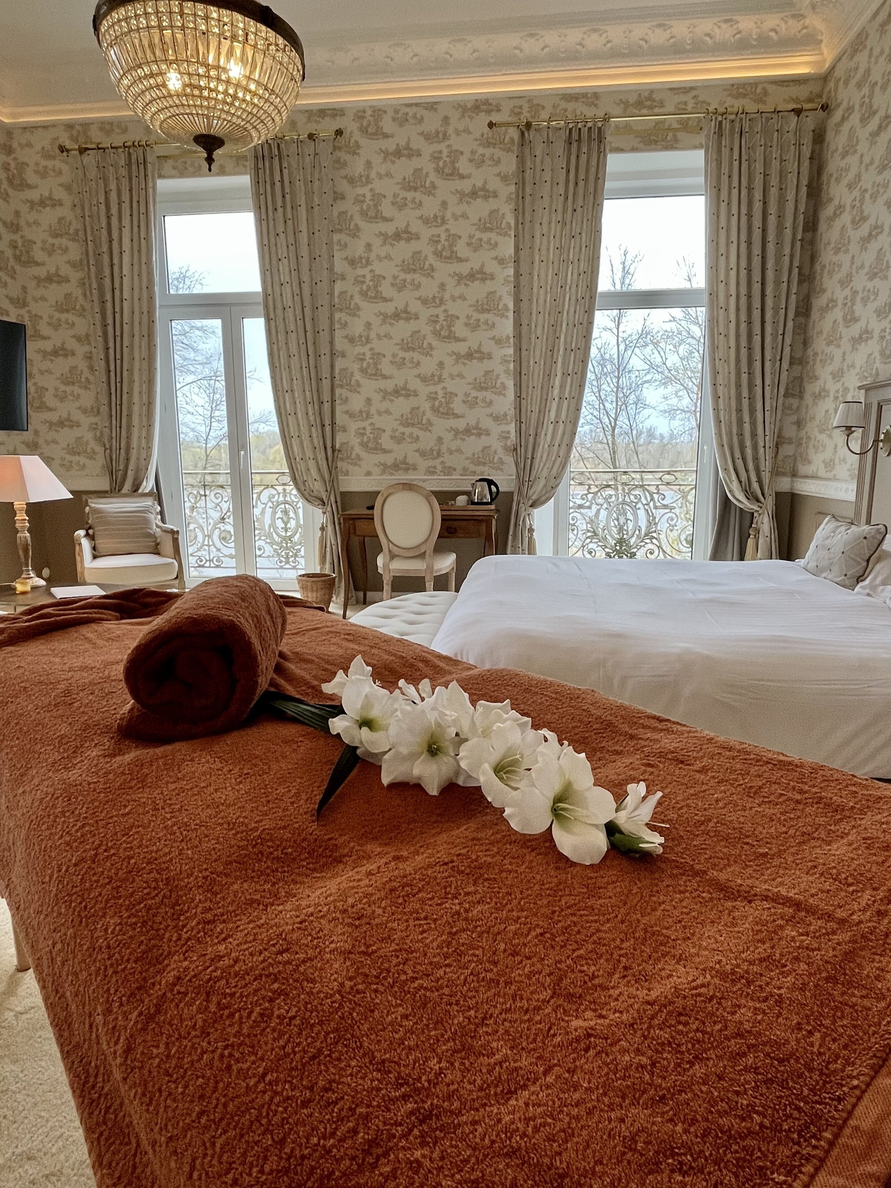 Une chambre d’hôtel avec un grand lit, un bureau, une chaise et un balcon avec des rideaux.