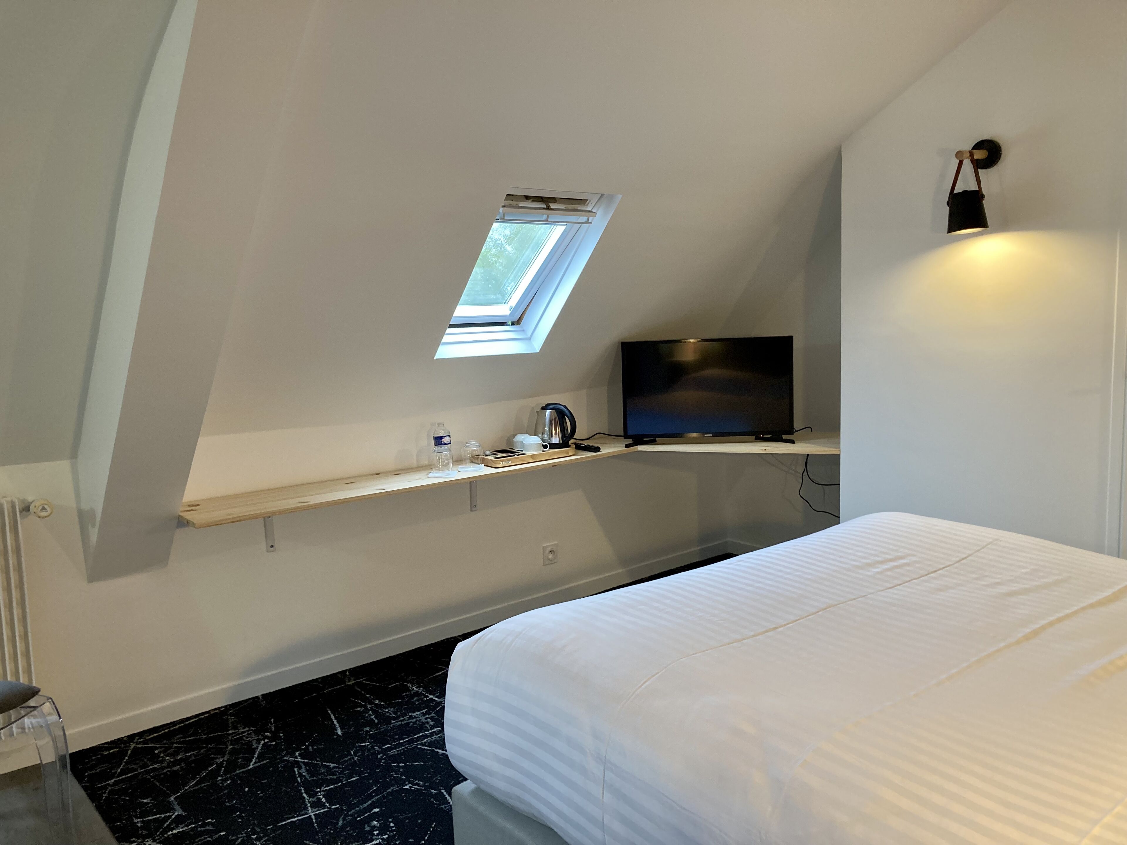 A bedroom with a bed, a TV on a shelf, a small window, and a radiator.