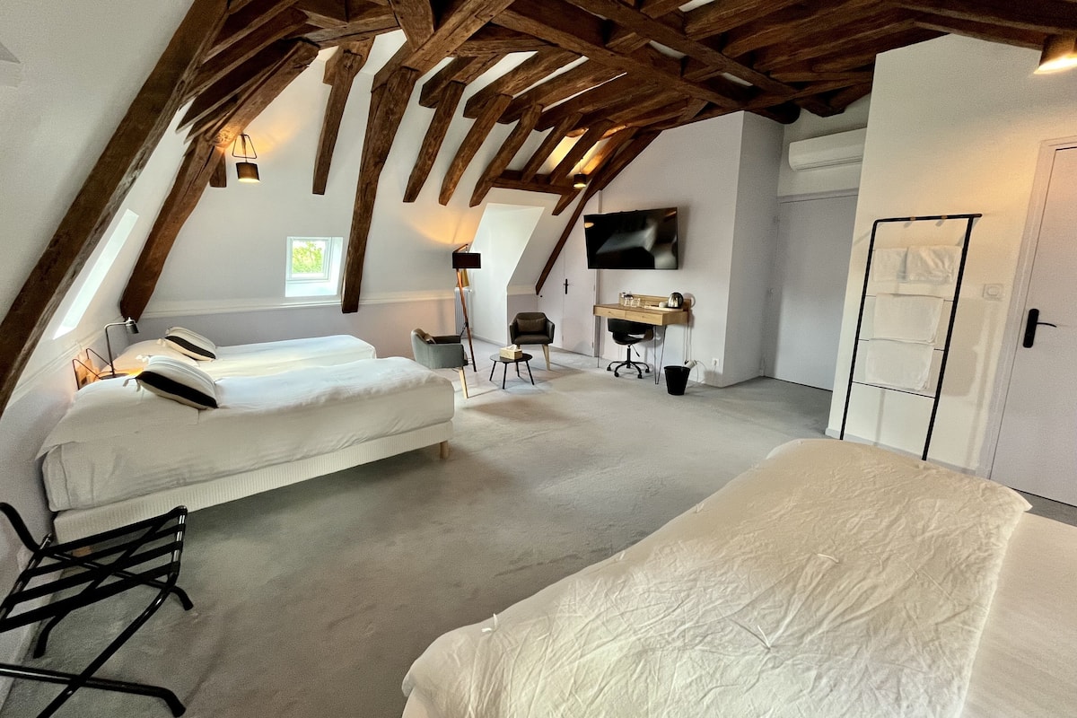 A spacious attic bedroom with a sloped ceiling, a bed, a desk, a chair, and a television.
