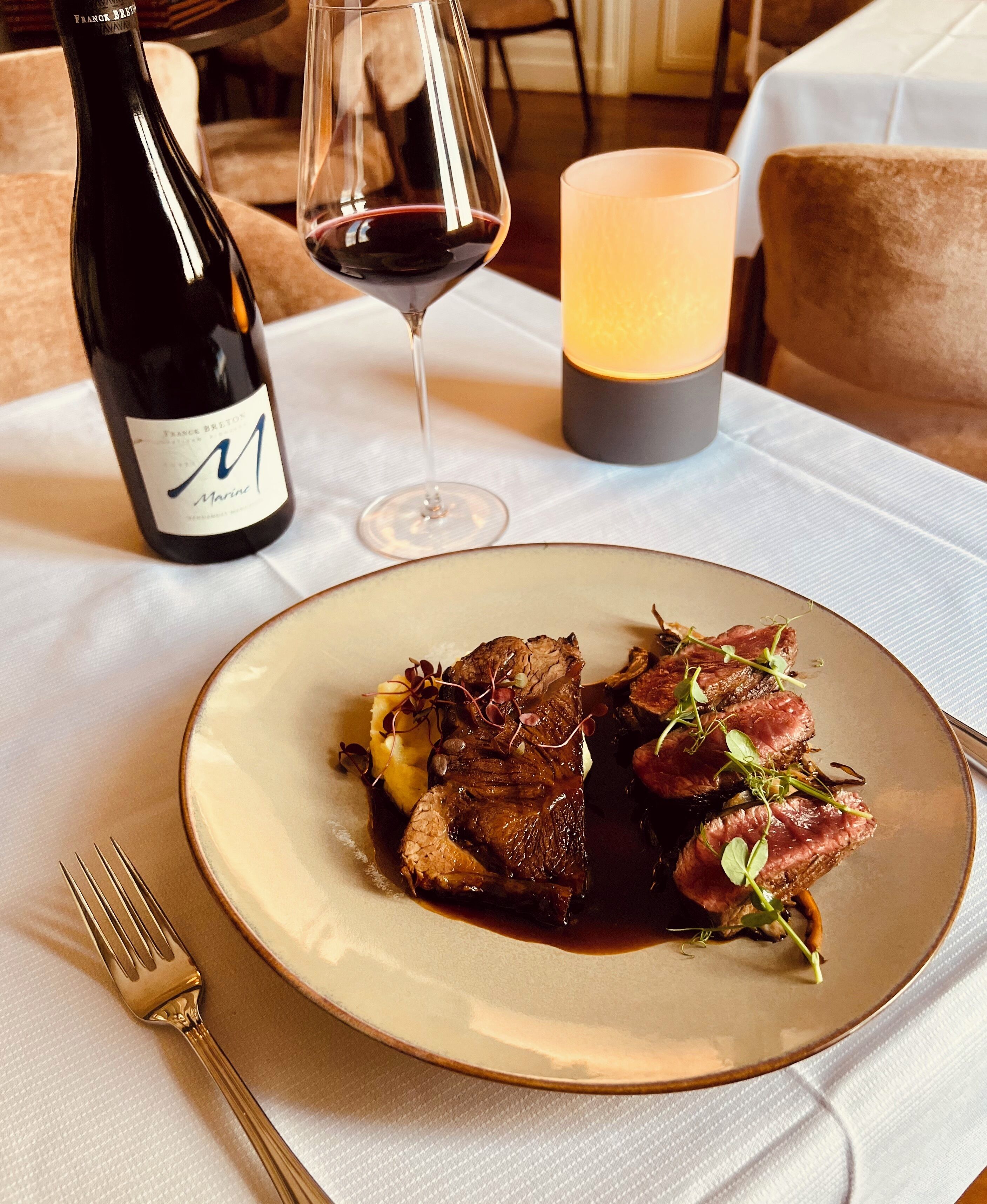 A dining table with a plate of food, a wine bottle, and a glass of wine.