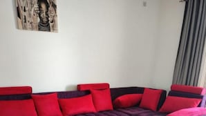 Un salon avec un canapé violet, des coussins rouges, une table basse en bois et un tapis rouge.