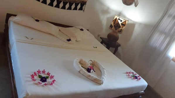 A neatly made bed with a white sheet, a decorative pillow, and a small flower arrangement. - Stay.Plus Malindi Apartment (Malindi)
